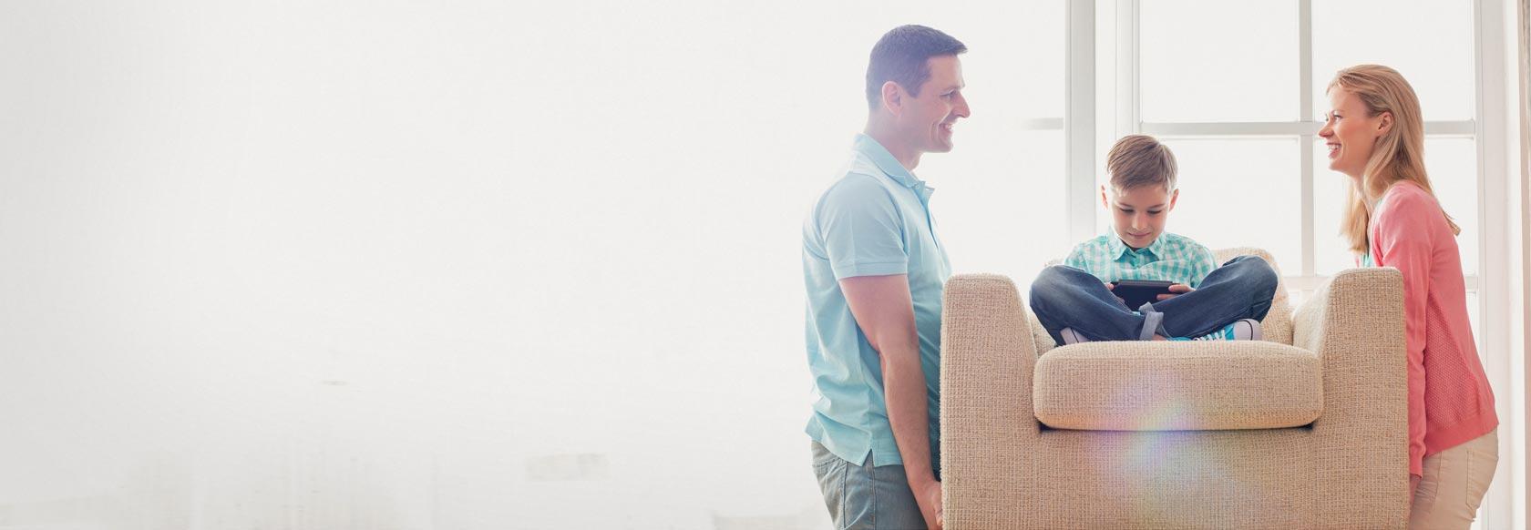 Mother and father moving couch with young son sitting on it, smiling